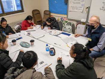 a group of learners work together at a table with a volunteer teacher