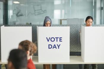 a woman in hijab and an Asian woman fill out voting ballots behind partitions