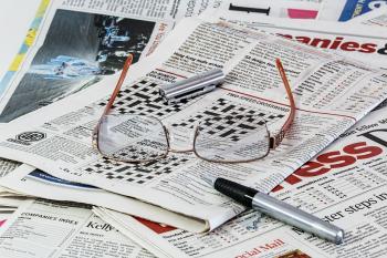 newspaper crosswords with a pair of glasses and a pen